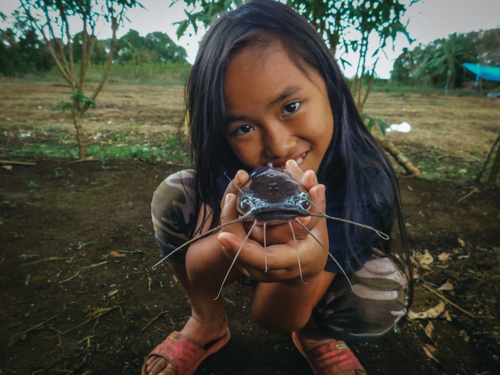 Meisy is crouching down to the camera and showing off a big catfish.